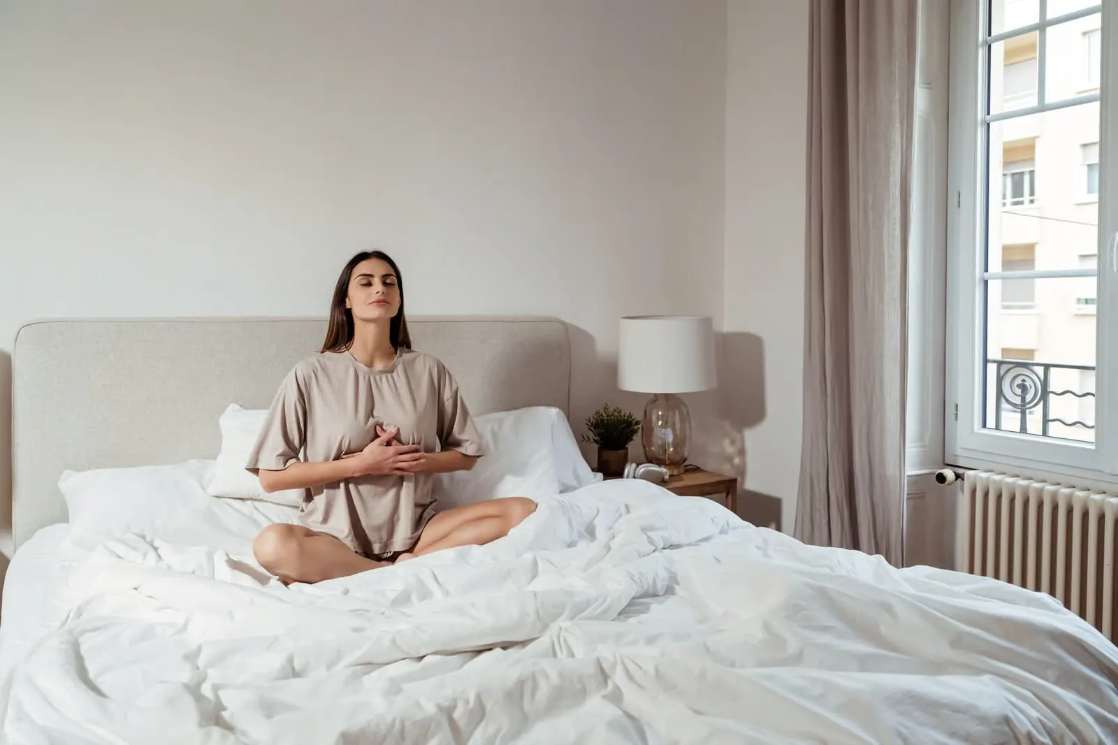 Woman sitting on her bed with hands at her chest, practicing slow breathing