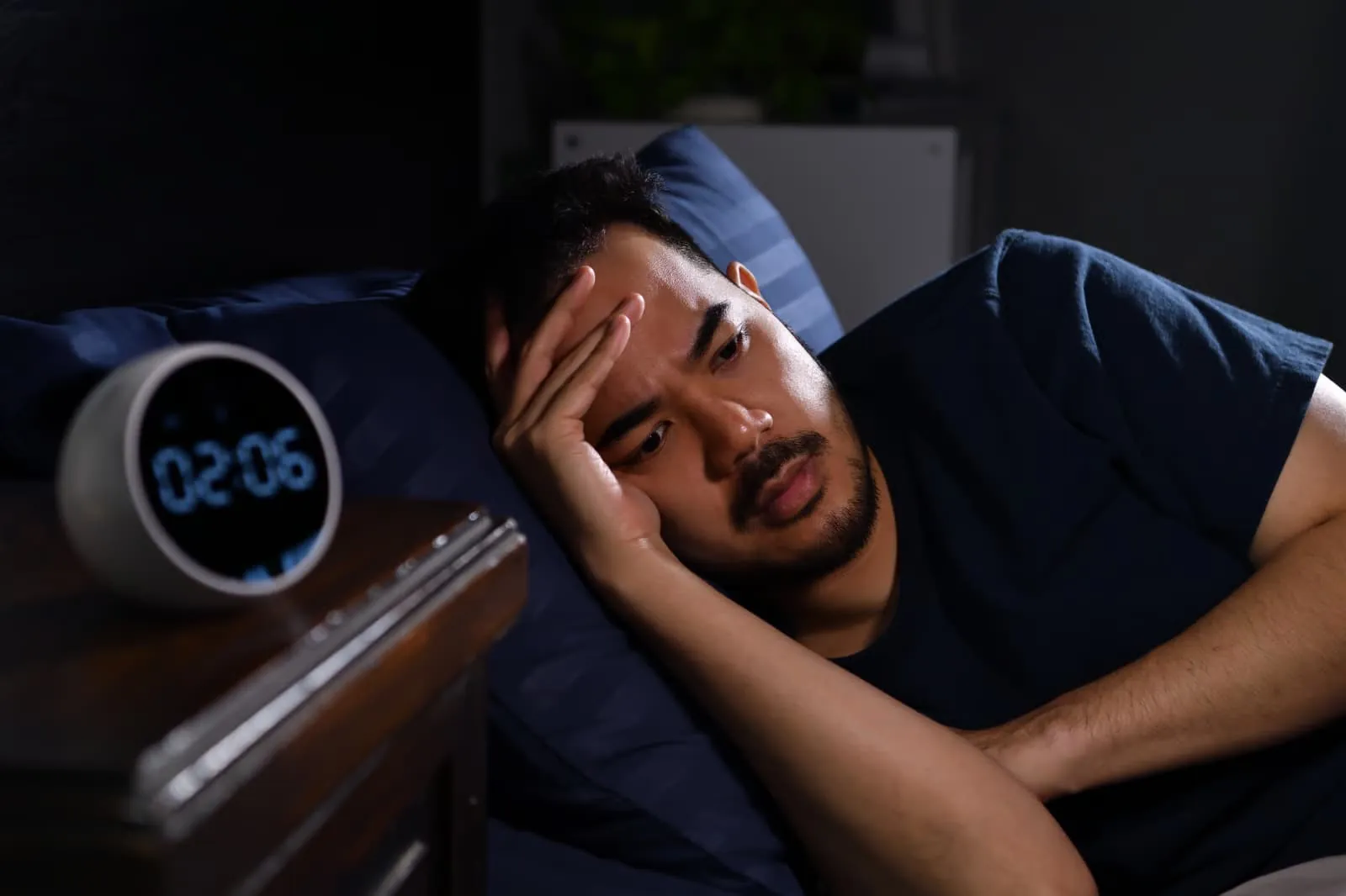 Man lying awake in a dark bedroom next to a digital clock